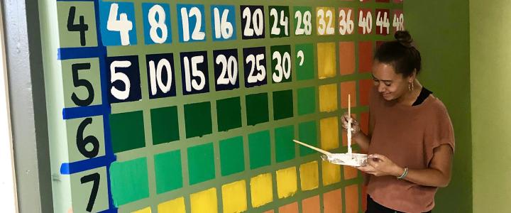Julia Miller painting a colorful times table on a hall wall.