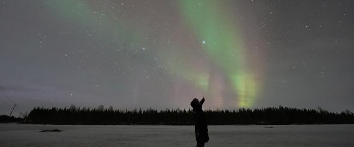 Person pointing Aurora Borealis on the sky during a dark night