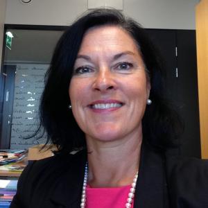Kristina Kaihari smiling at camera. She has dark hair and is wearing a dark pink blouse and black jacket.