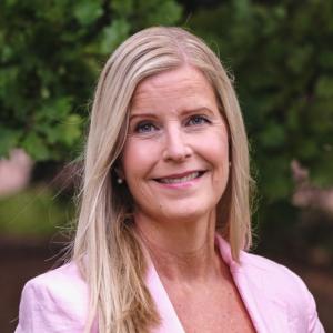Woman with blonde shoulder length hair and pink suit jacket smiling at the camera