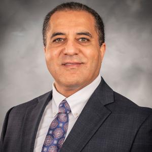 Person in black suit in front of a gray background