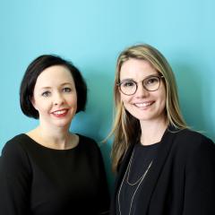 Emilie Gardberg and Laura Hirvi smiling at the camera in front of a turquoise wall