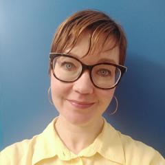 Woman with short brown hair, glasses and a yellow shirt