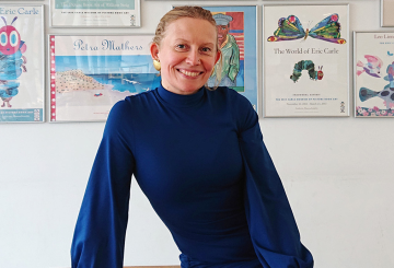 Pirita Tolvanen sitting by a desk with posters behind her on a wall